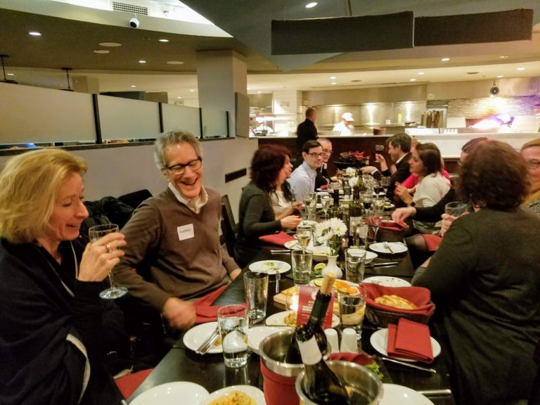 Laughing group drinking and eating at a long table in a restaurant